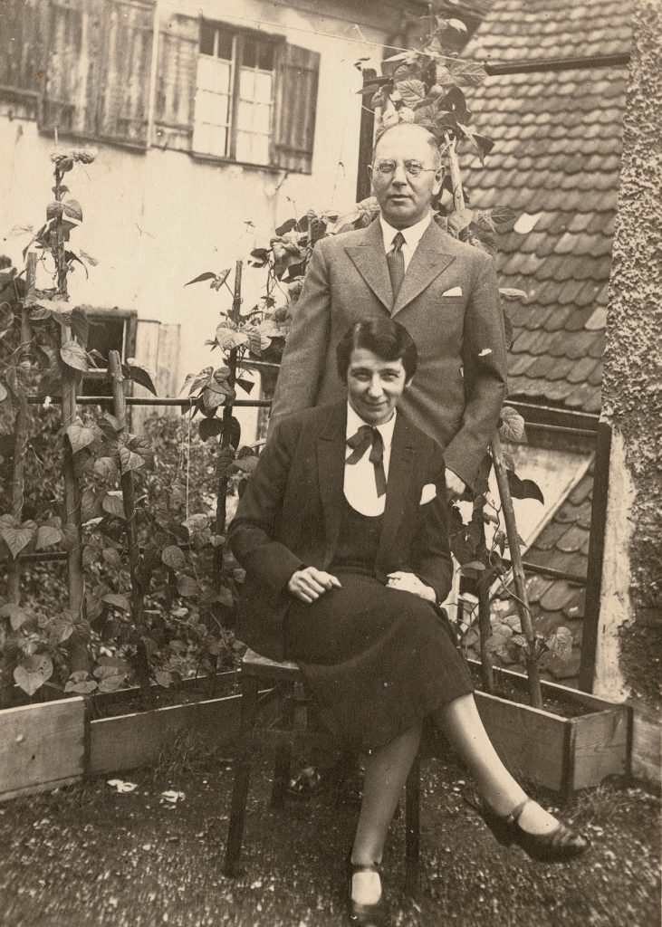 A black and white photo of Jakob Feibelmann standing and his wife Irma sitting in front of him on a balcony.