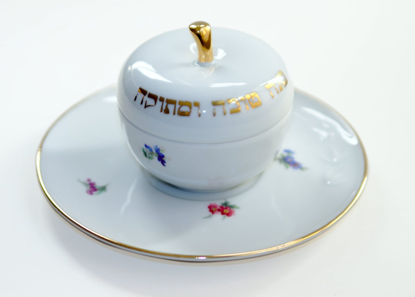 Eine Dose aus weißem Porzellan bemalt mit bunten Blümchen und einer hebräischen Aufschrift
