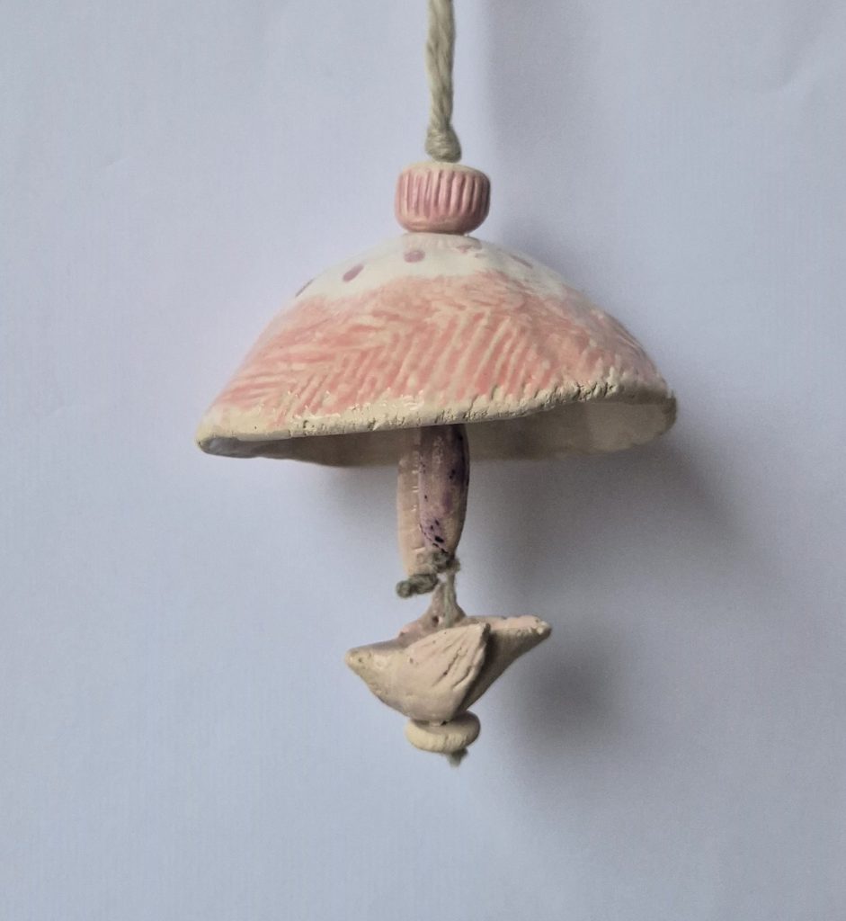 Eine getöpferte Glocke, darunter eine Taube aus Ton. Beides an einem Faden.