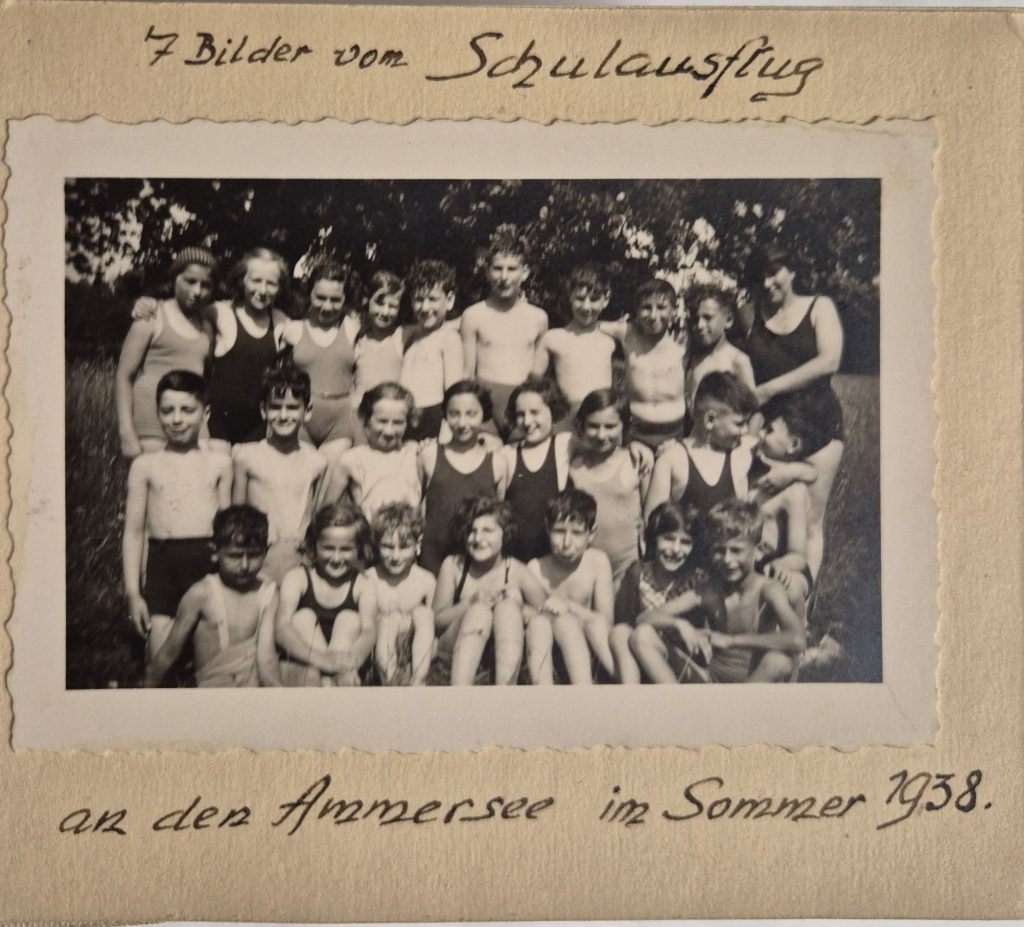 Schwarz-weiß Foto von knapp 20 Kindern, die alle in die Kamera schauen, in einem Album. Darüber und darunter steht: 7 Bilder vom Schulausflug an den Ammersee im Sommer 1938.